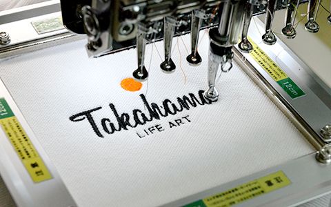 刺繍機と、Tシャツに刺繍されたタカハマライフアートのロゴのオリジナルデザイン