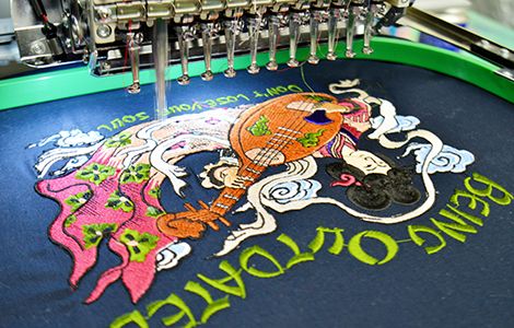 刺繍機と、Tシャツに刺繍された三味線を持った女性のカラフルなオリジナルデザイン